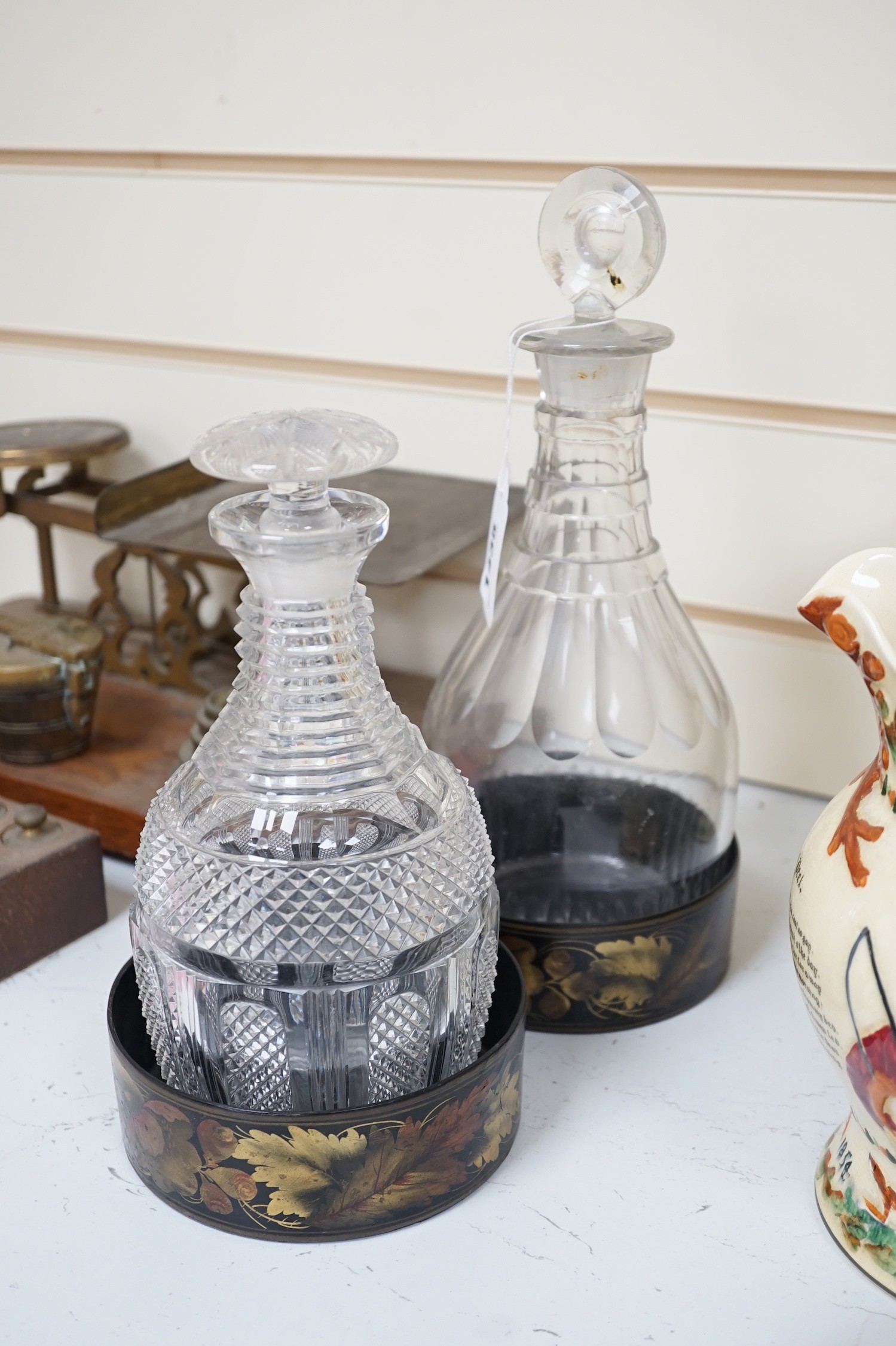 Two Regency cut glass decanters and stoppers and a pair of papier maché wine coasters, tallest 30 cm
